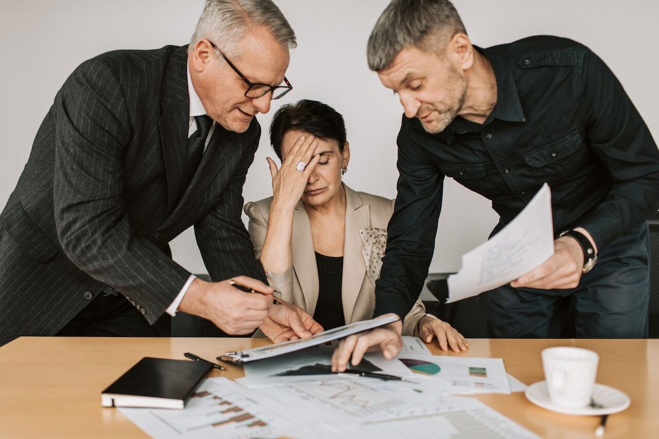Two businessmen stand over a business woman who appears overwhelmed - Photo by Vlada Karpovich